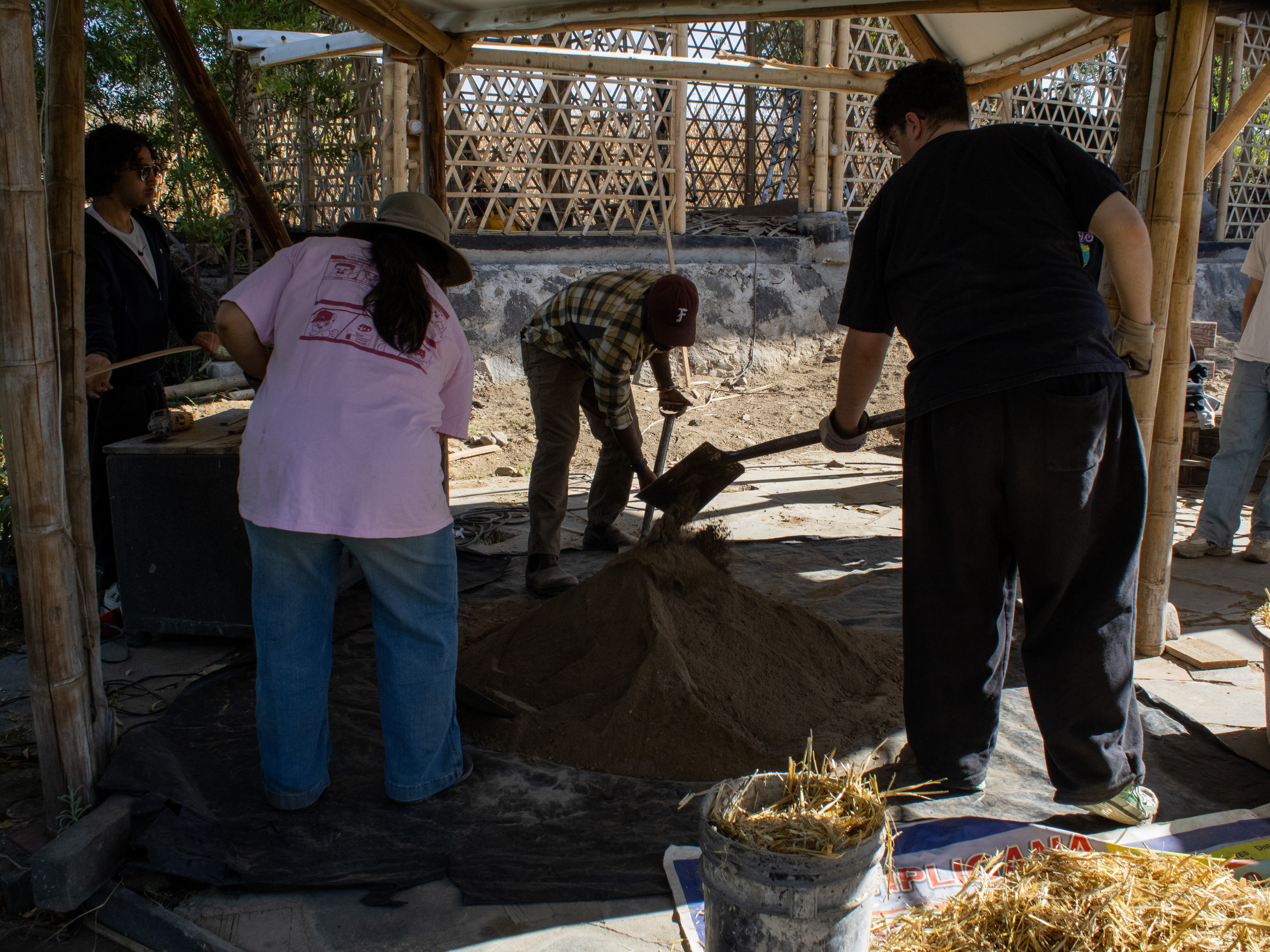 Volunteers shovelling sand inside a bamboo pavilion